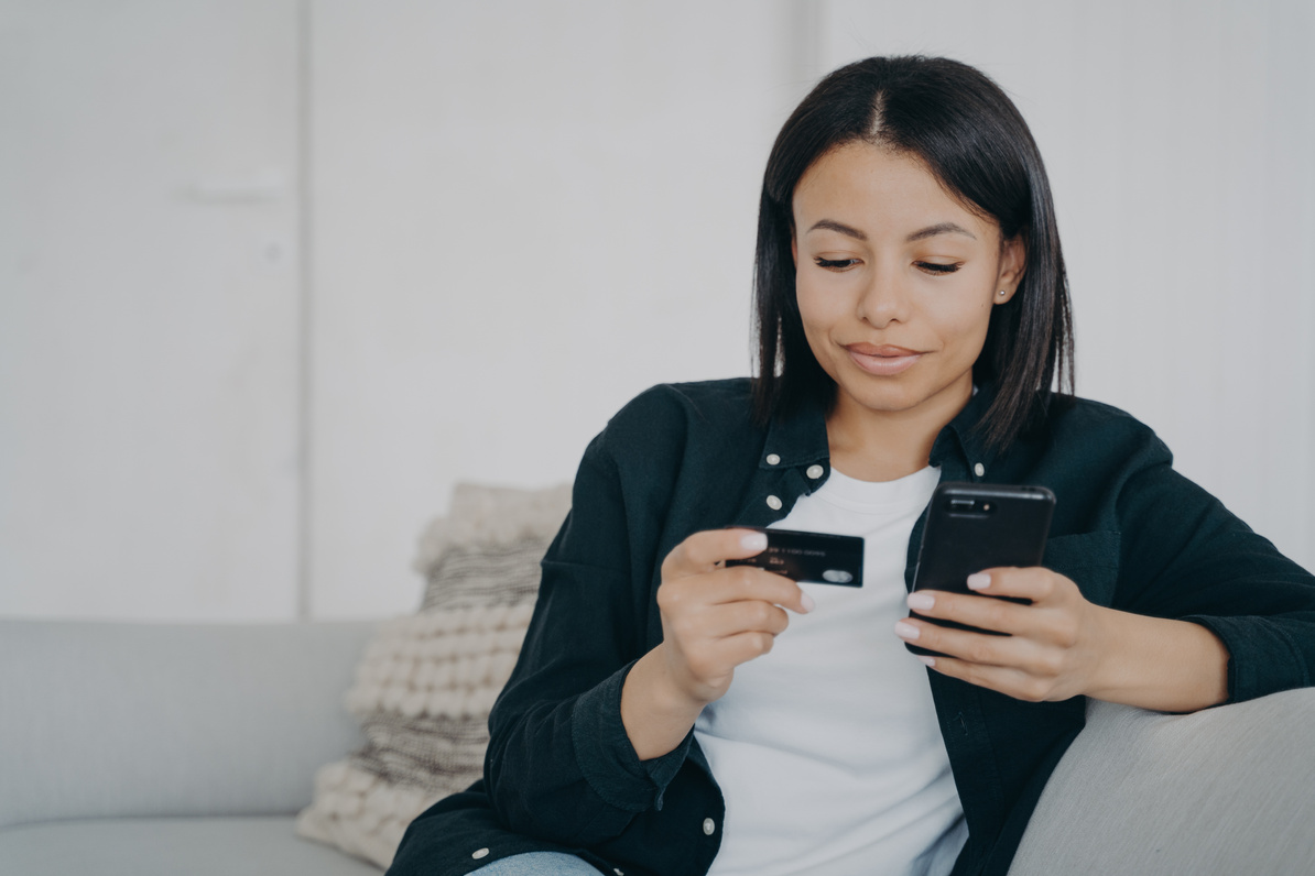 Online banking. Female holds credit card, phone, makes money transfer using mobile bank app at home